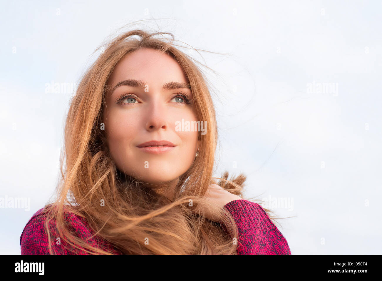 Serene beautiful woman with long hair fluttering in the wind. Outdoor portrait. Looking up at the distance, low point view Stock Photo