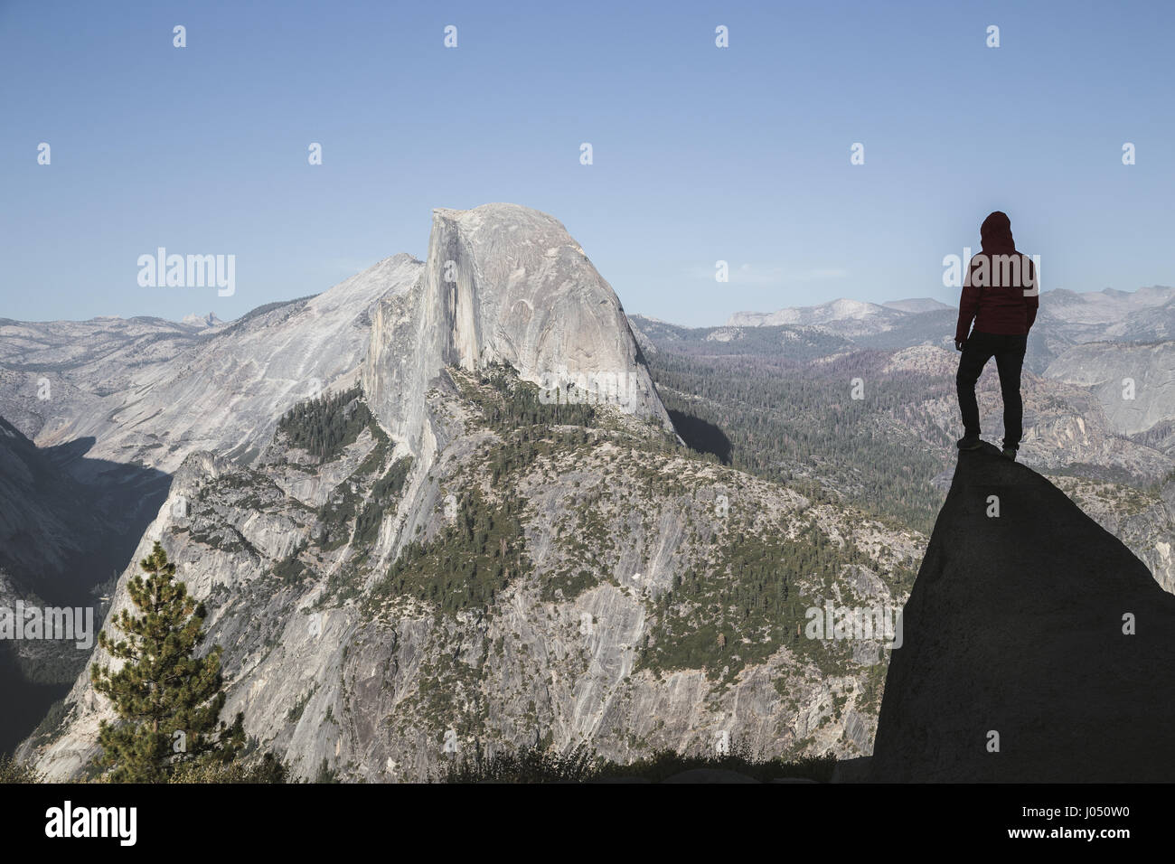 A young hiker is standing on a rock enjoying the view towards famous Half Dome at Glacier Point at sunset, Yosemite National Park, California, USA Stock Photo
