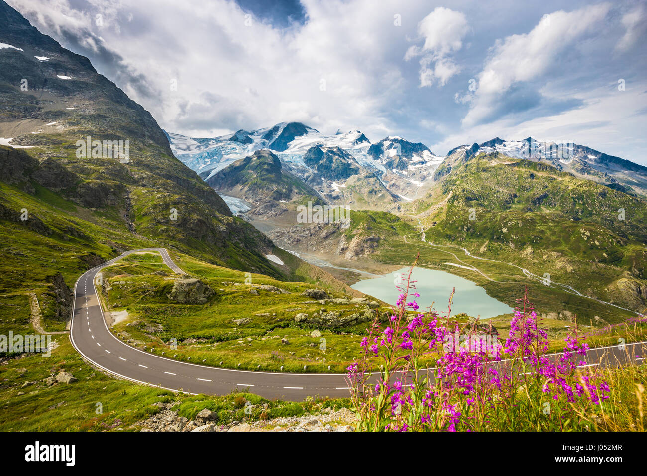 Beautiful view of winding mountain pass road in the Alps running through idyllic alpine scenery with mountain peaks, glaciers, lakes and green pasture Stock Photo