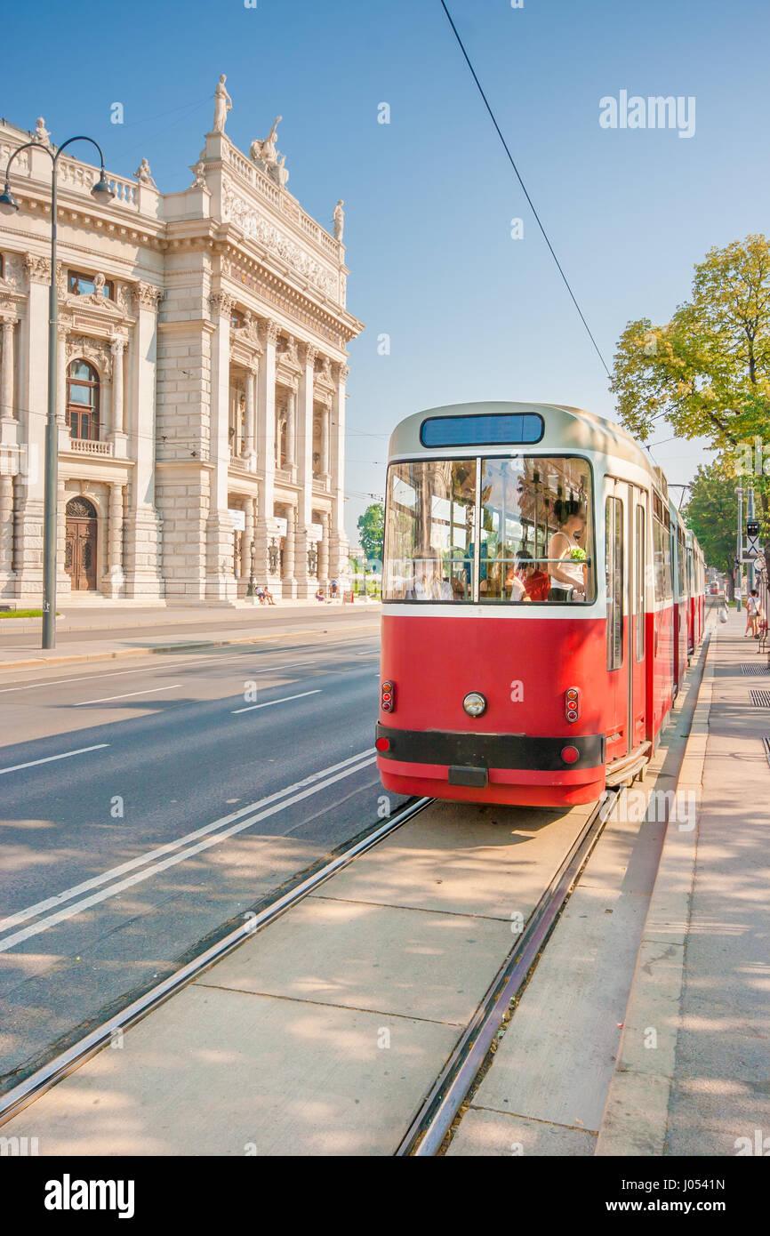 Classic view of famous Wiener Ringstrasse with historic Burgtheater (Imperial Court Theatre) and traditional red electric tram on a beautiful sunny da Stock Photo