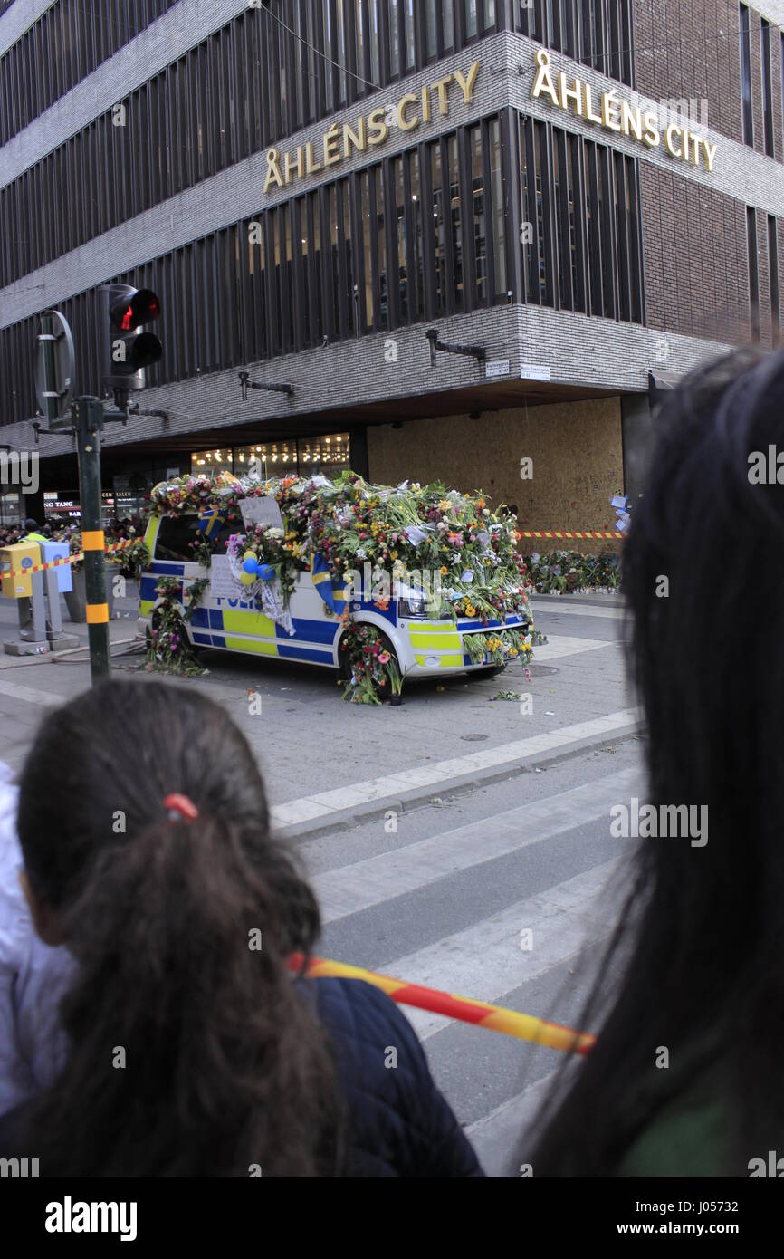 Pedestrians looking on the hit spot location in Ahlens mall, with Swedish Polis, police car in the background, covered with pileup flowers in sympathy of the Swedes nation to the casualties of the 7 April 2017, Stockholm terrorism attack, Stockholm, Sweden. Stock Photo