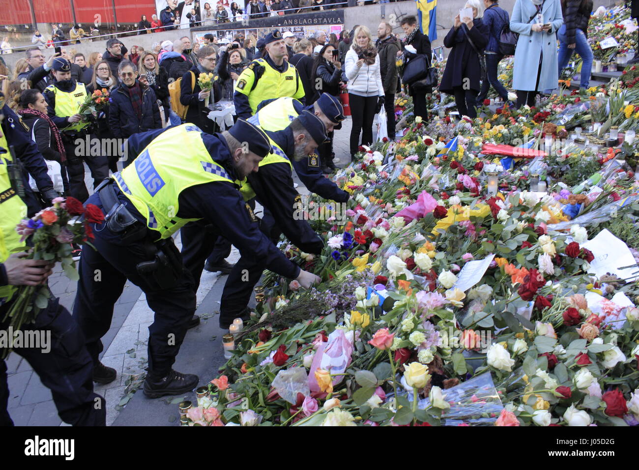 Stockholm, Sweden. 10th April, 2017. Swedish police (Polis) officers paying honor to the Stockholm terrorist attack casualties, by laying flowers at Sergels Torg square stairway, hidden under the piled colurful flowers,  condolences, hope messages, Swedish flags and burning candles. Stockholm, Sergels Torg square, Sweden Credit: BasilT/Alamy Live News Stock Photo