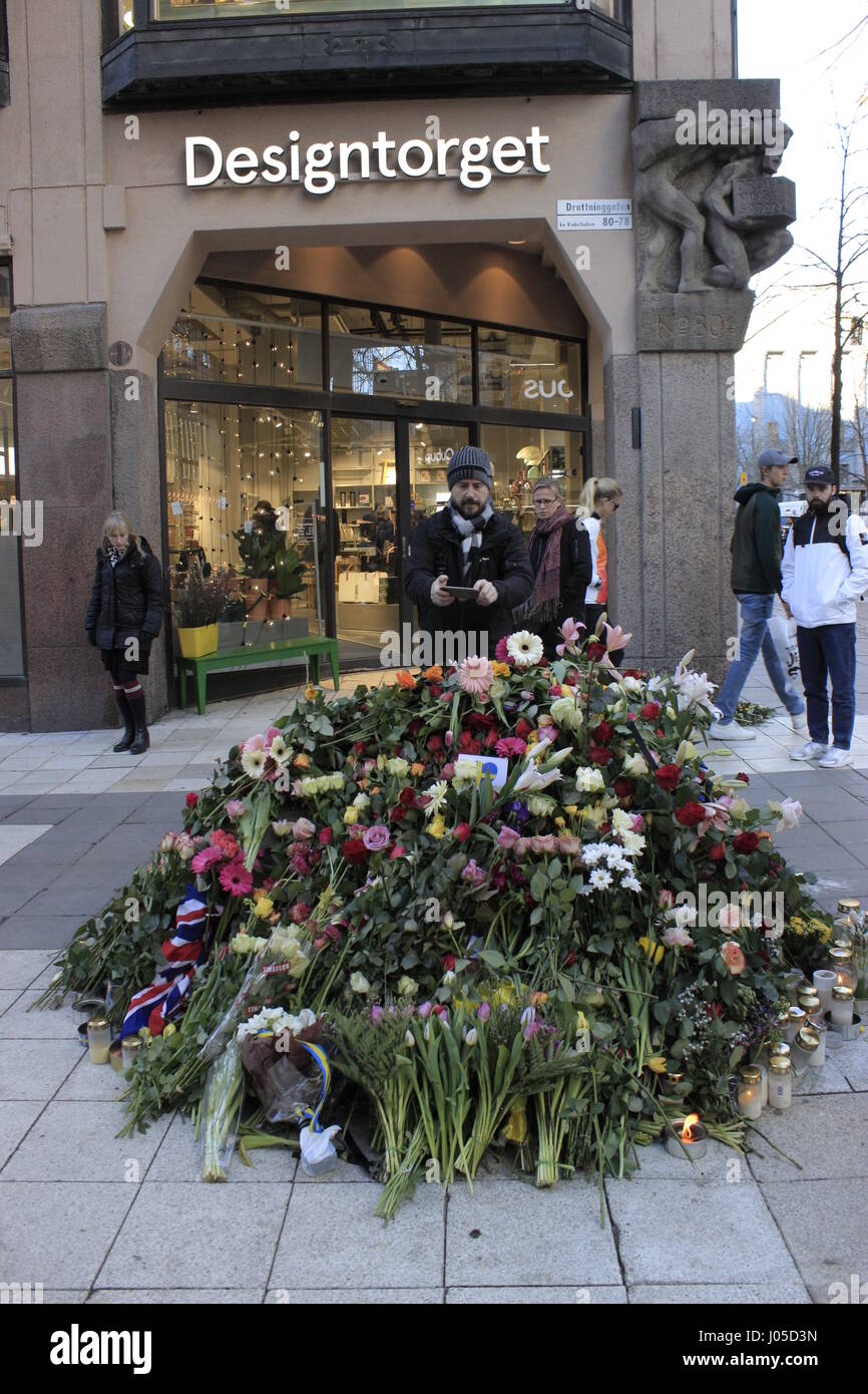 Stockholm, Sweden. 10th April, 2017. Side view of the concrete barricade depicting a lion animal, is hidden below a pile of flowers bouquetes and burning candles with a British flag dedicated to the British casualties in Drottninggatan street accessed by pedestrians. Stockholm city centre. Sweden Credit: BasilT/Alamy Live News Stock Photo