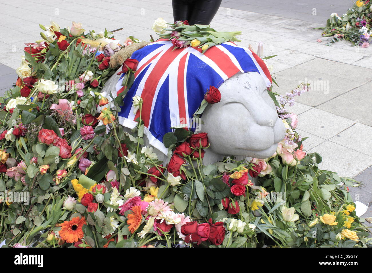 Stockholm, Sweden. 11th April, 2017. Side view of British flag & fresh flower bouquets surrounding the concrete lion's head street barricade,at the corner of 78 Drottninggatan & Kungsgatan streets, in remembrance of the British citizen Chris Bevington. another casualty of the Stockholm's terrorist truck attacker. Stockolm city, Sweden. Credit: BasilT/Alamy Live News Stock Photo