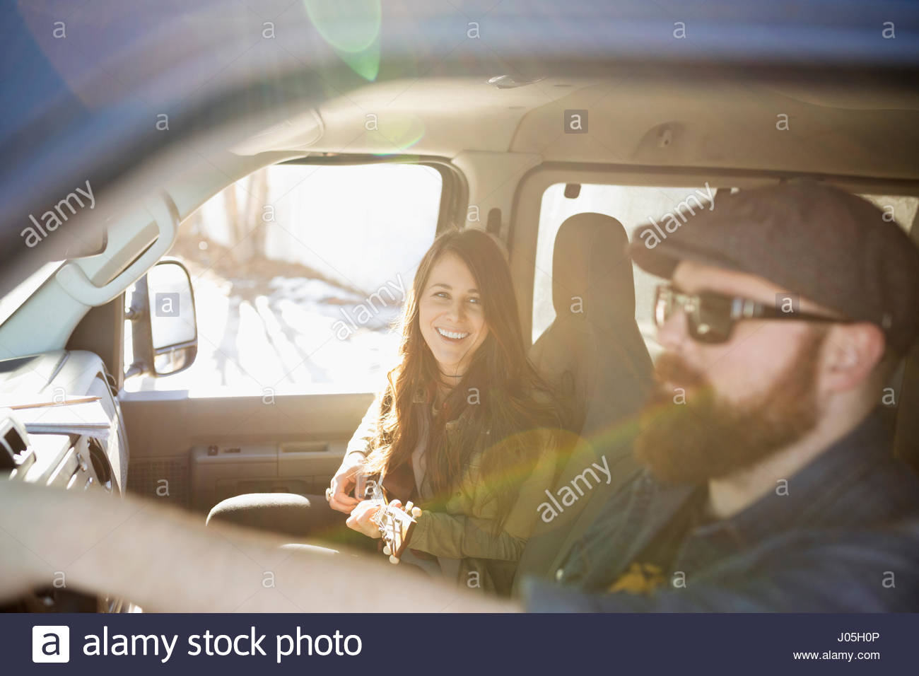 Young woman playing ukulele, riding in sunny van with boyfriend Stock