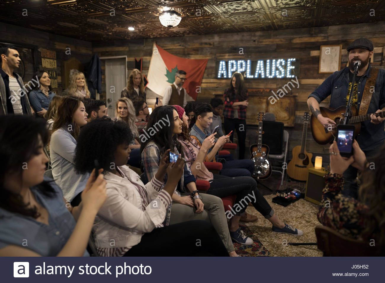Audience with camera phones photographing musician playing guitar and singing on garage stage Stock Photo