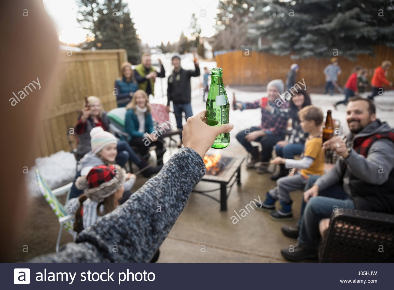 Woman with beer bottle toasting family and neighbors at fire pit in