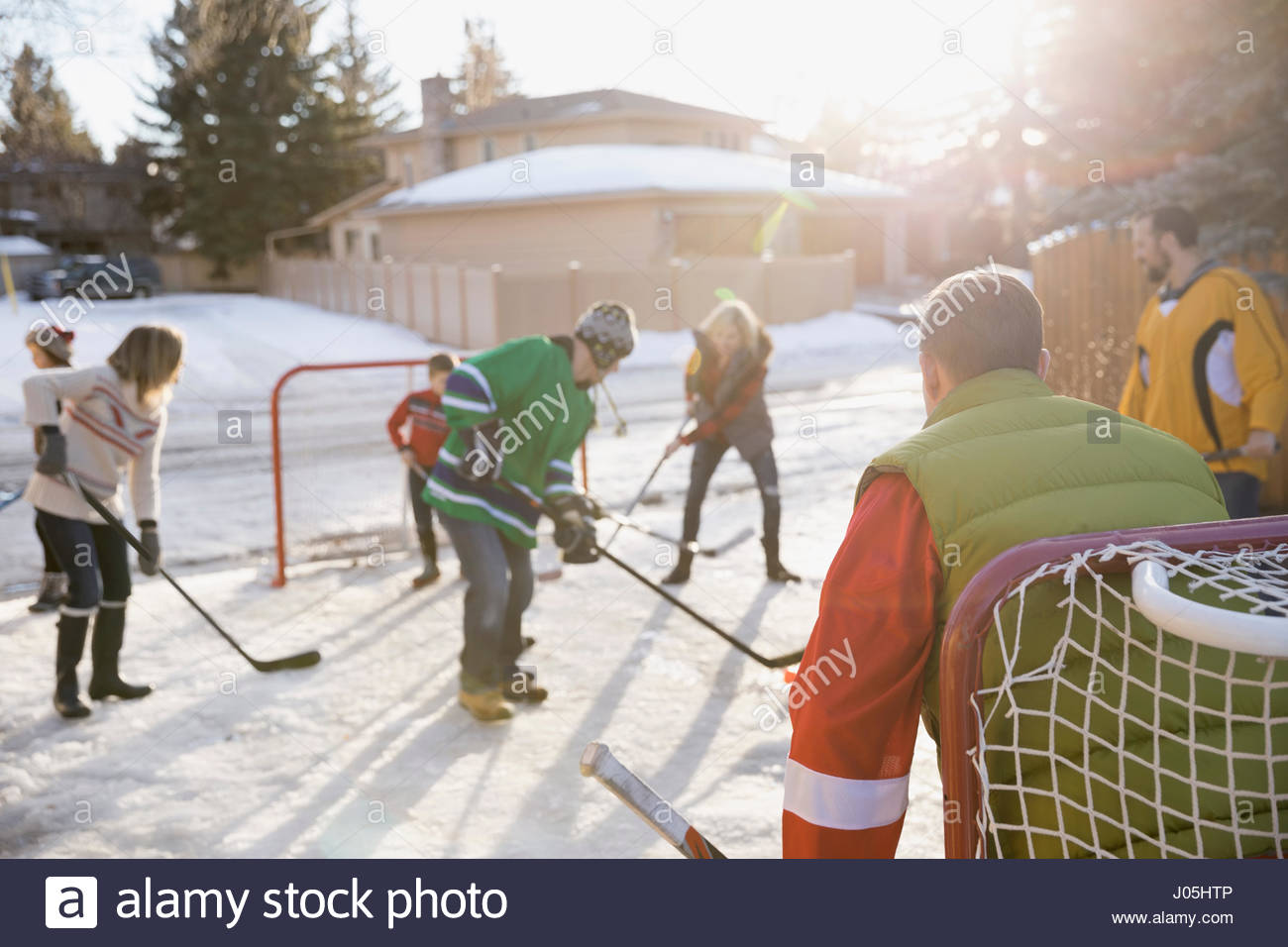 Families playing ice hockey in sunny, snowy driveway Stock Photo Alamy