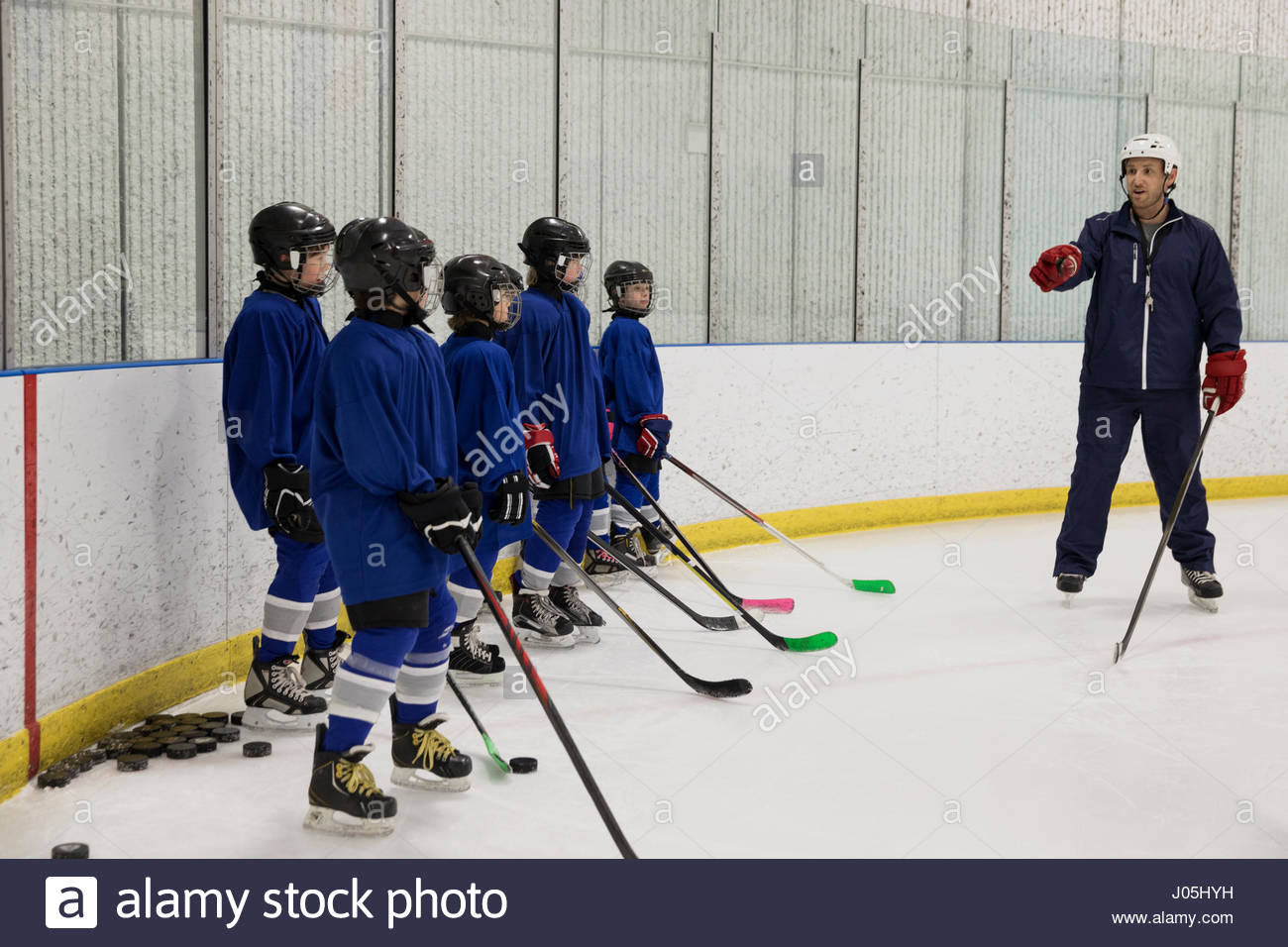 Boy ice hockey players listening to coach at practice on ice hockey