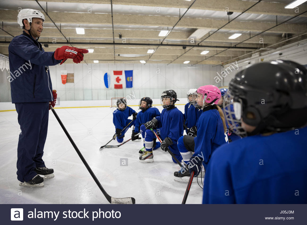 Male coach guiding boy and girl ice hockey players on ice hockey rink