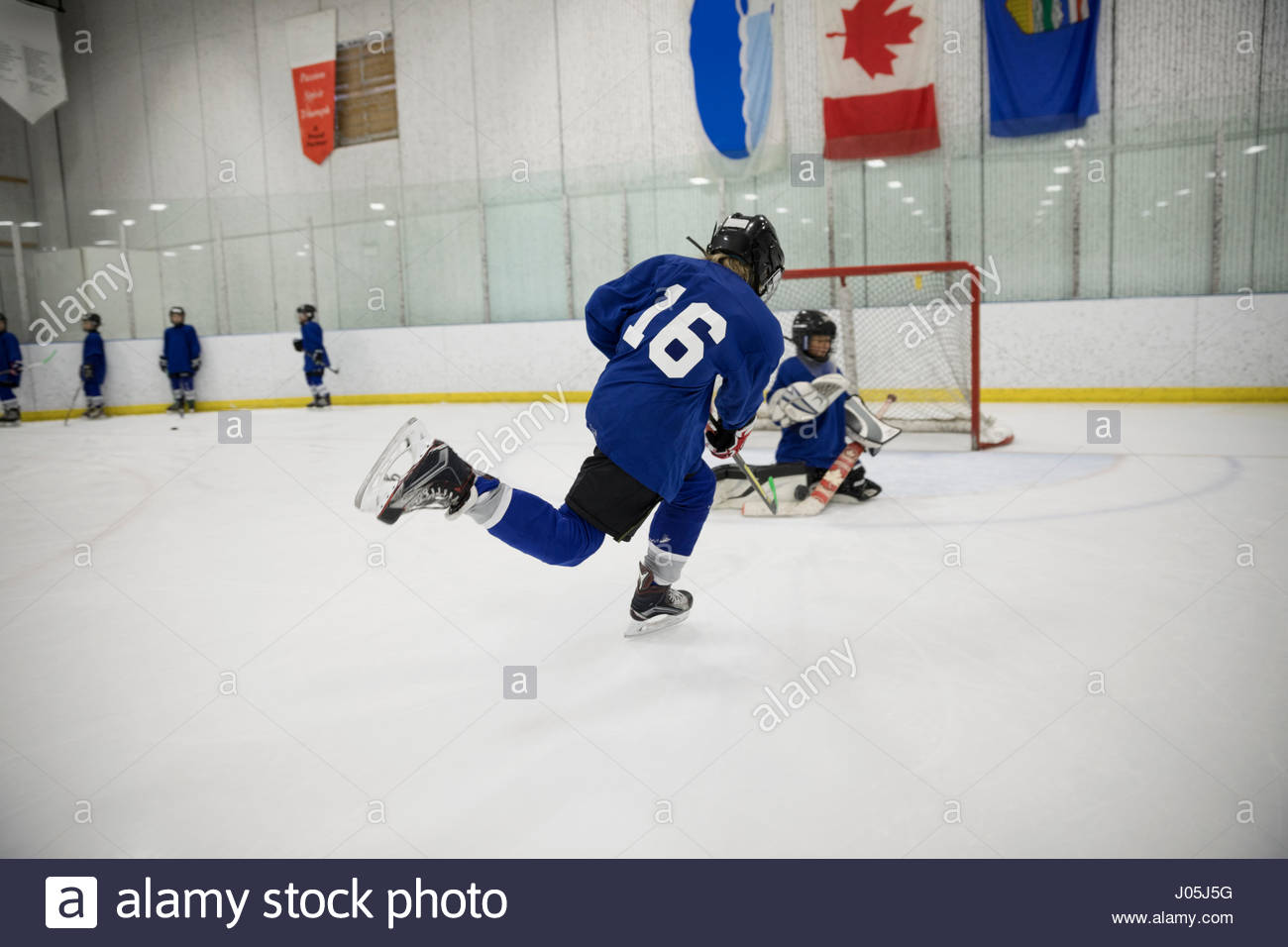 Boy ice hockey player taking a shot at goal on ice hockey rink Stock