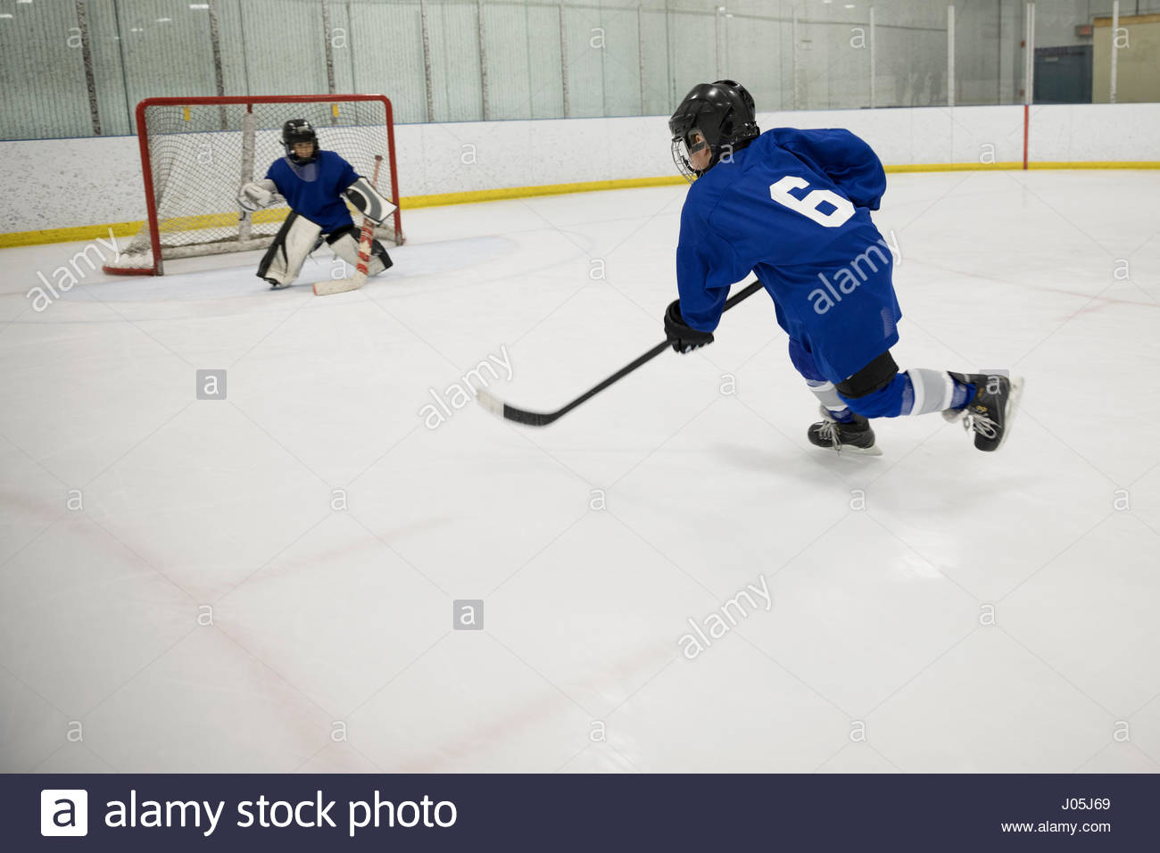 Boy ice hockey player taking a shot at goal on ice hockey rink Stock