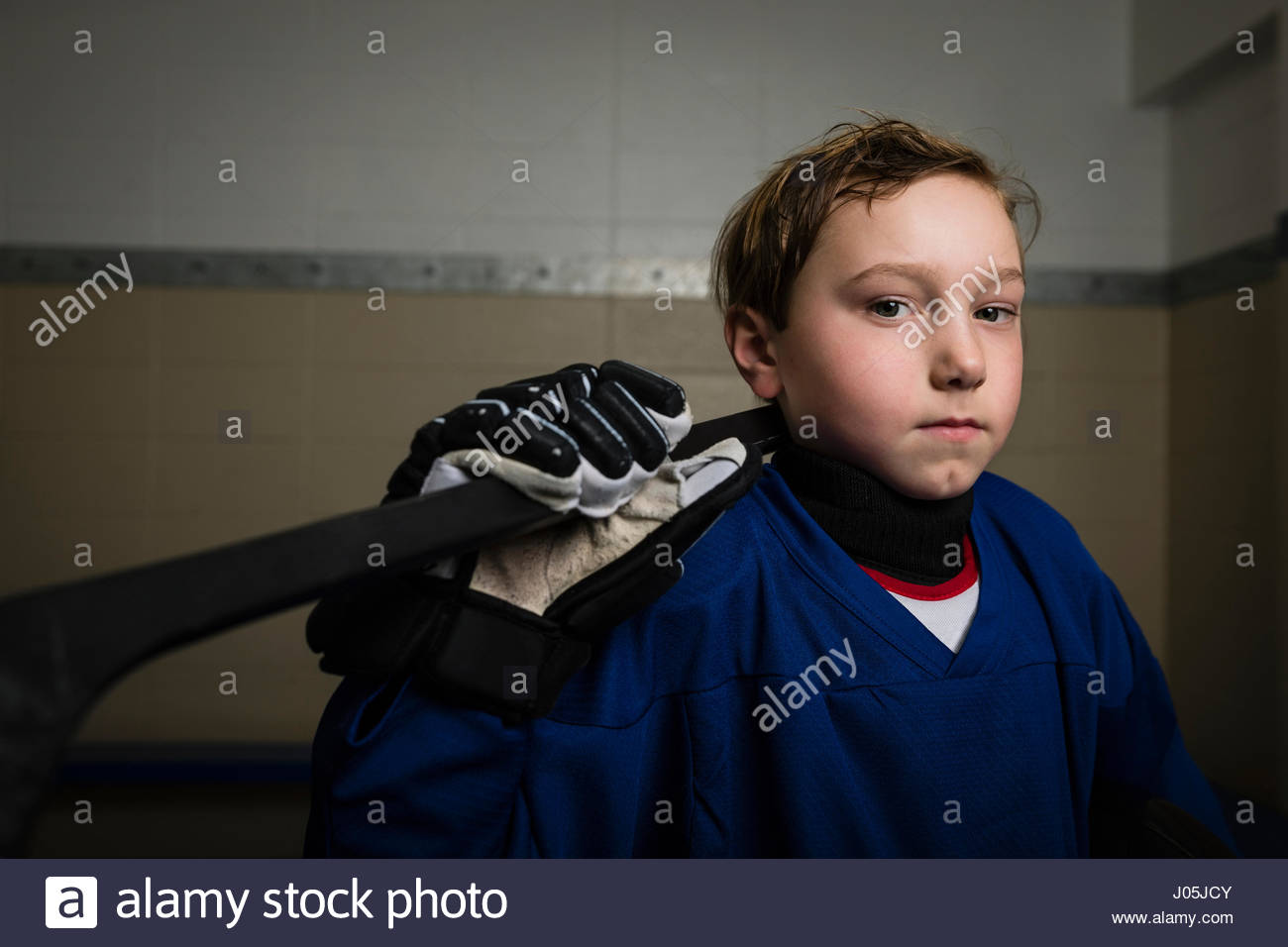 Portrait serious boy ice hockey player in uniform holding hockey stick