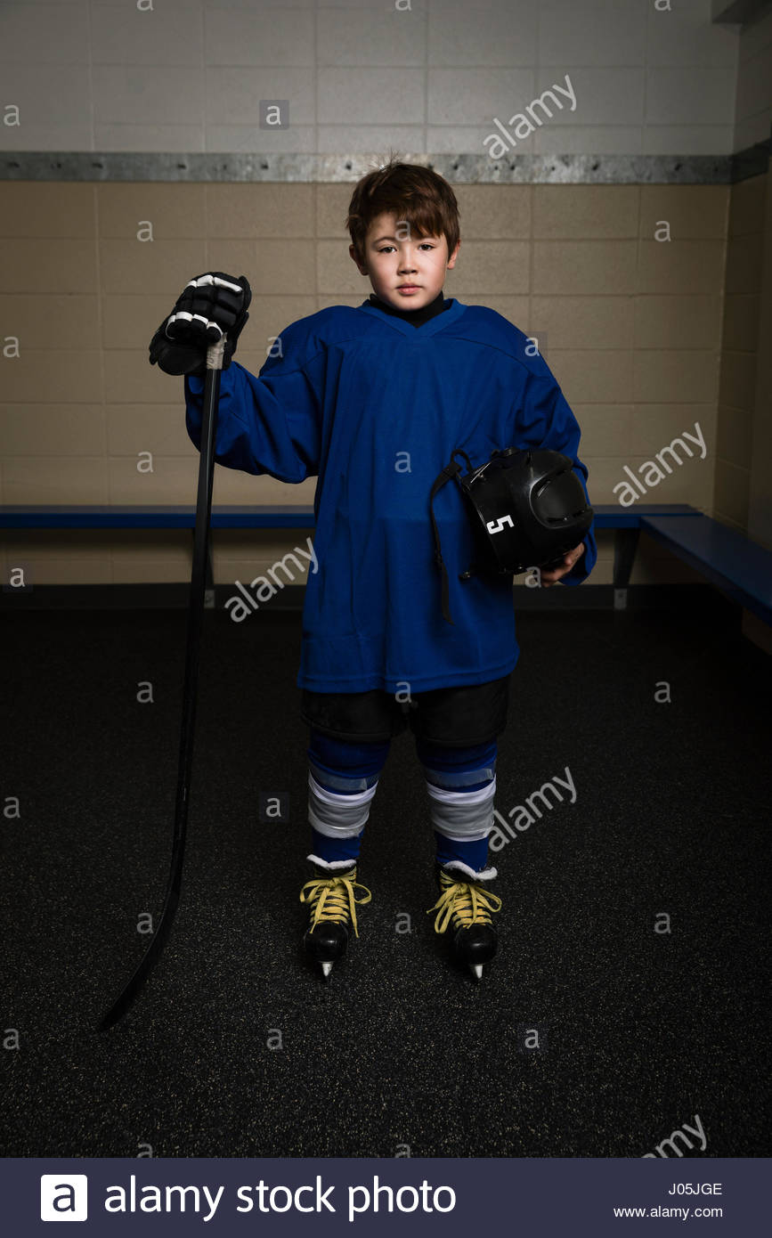 Portrait serious boy ice hockey player in uniform holding hockey stick