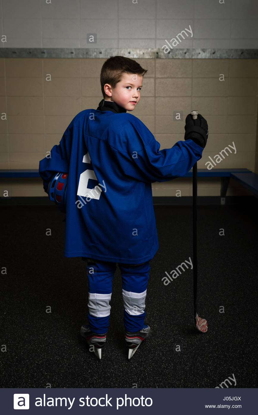 Portrait serious boy ice hockey player in uniform holding hockey stick