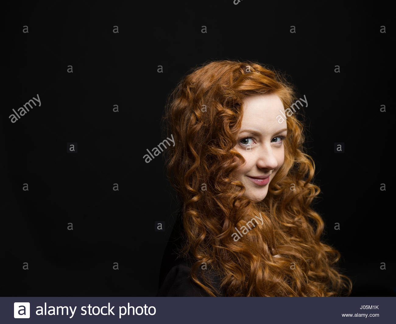 Portrait smiling woman with long curly red hair against black