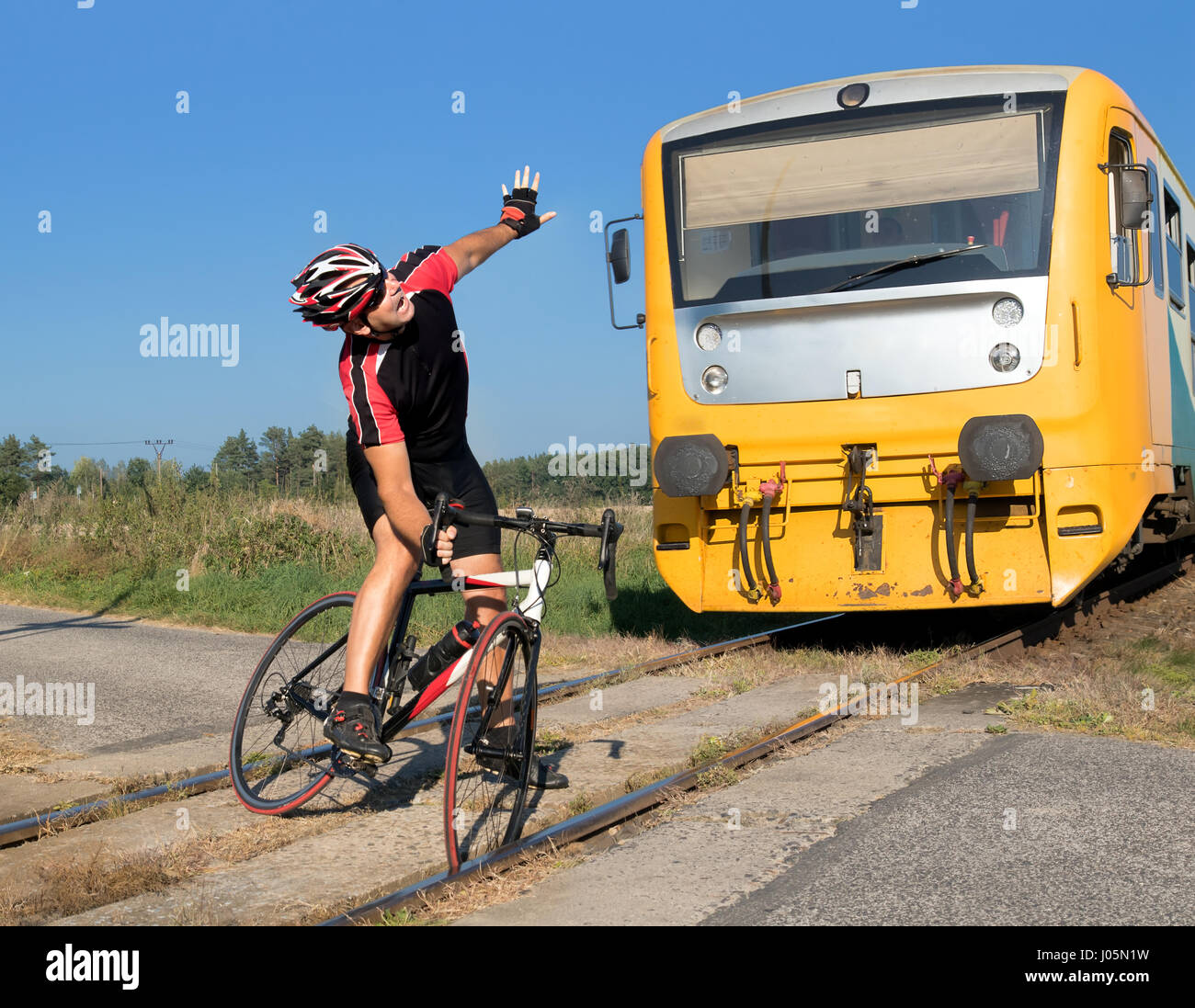 Unhappy cyclist has trouble on the railway crossing on Which the train is coming. The train goes to the cyclist stuck in the tracks. Stock Photo
