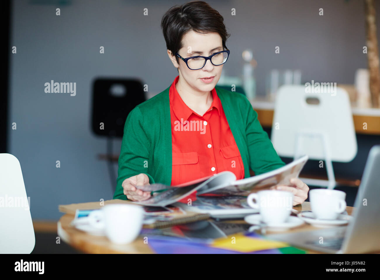 Portrait of young successful businesswoman wearing colorful casual clothes  reading magazines at table in cafe Stock Photo