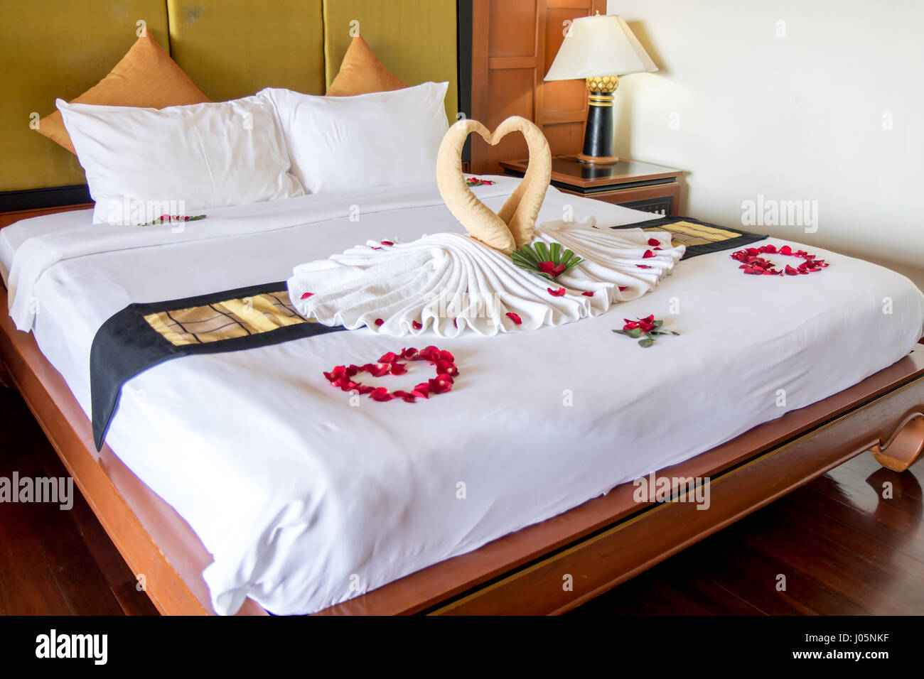Towel as birds decoration with red rose petals on white clean bed ...