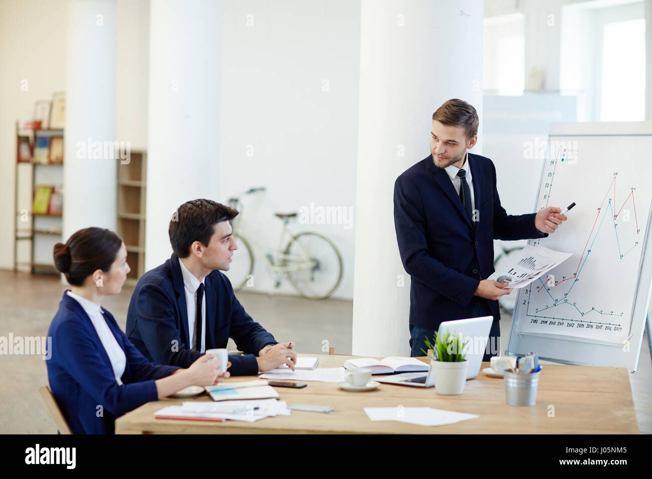 Businessman explaining graph on whiteboard and consulting colleagues ...