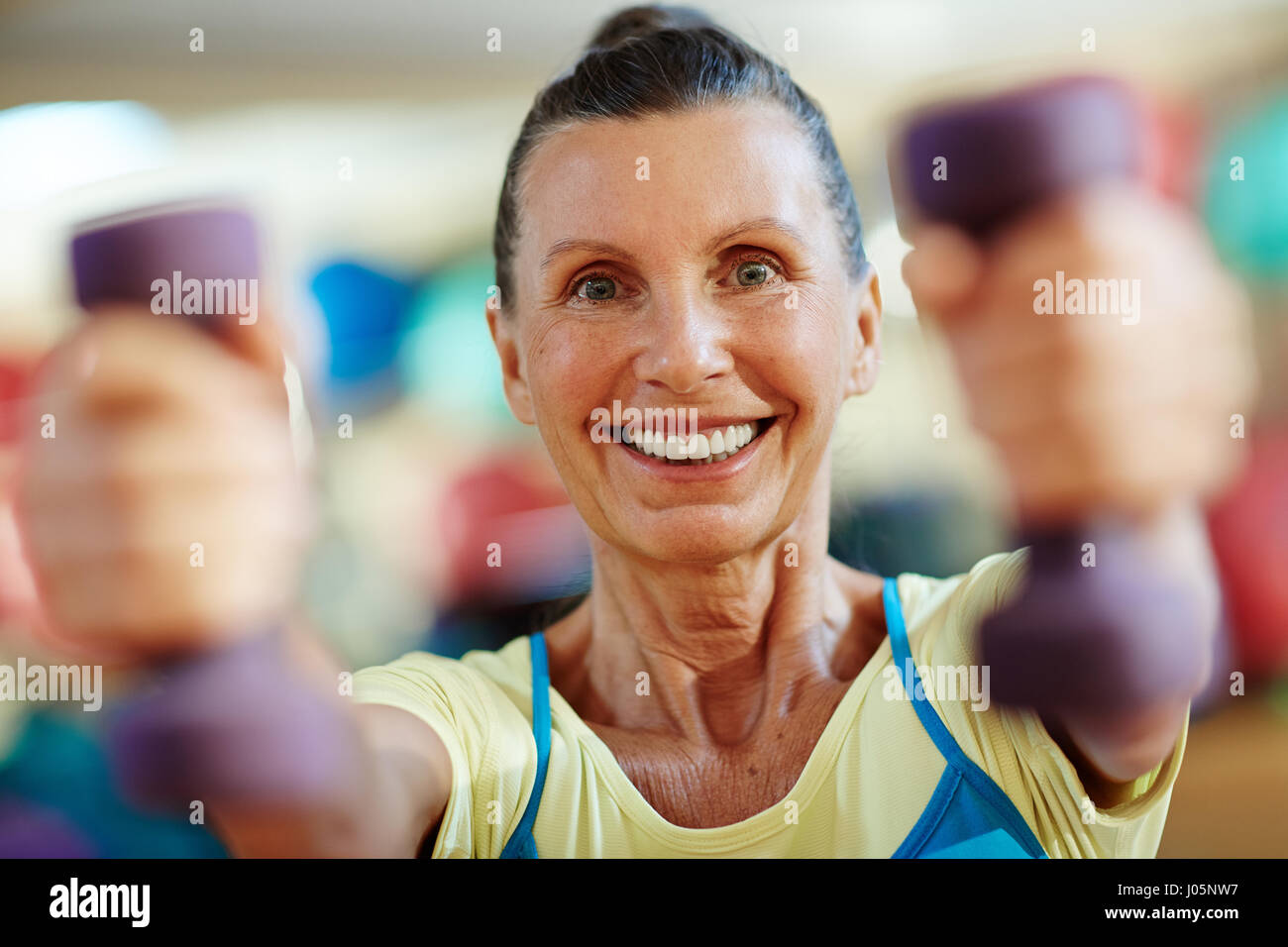Mature woman with toothy smile exercising with dumbbells Stock Photo