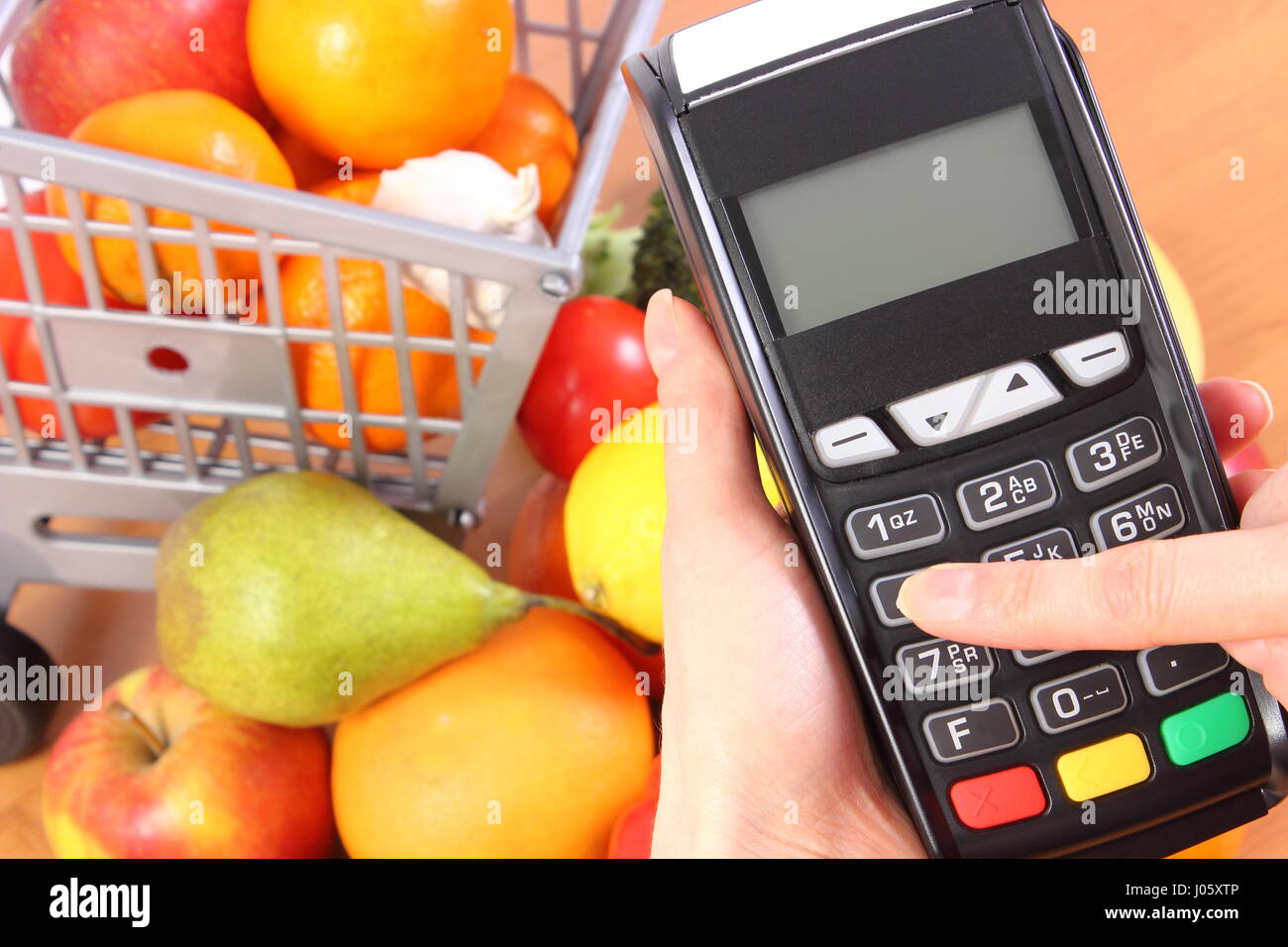 Hand of woman using payment terminal, enter personal identification number, credit card reader and fresh fruits and vegetables with plastic shopping c Stock Photo