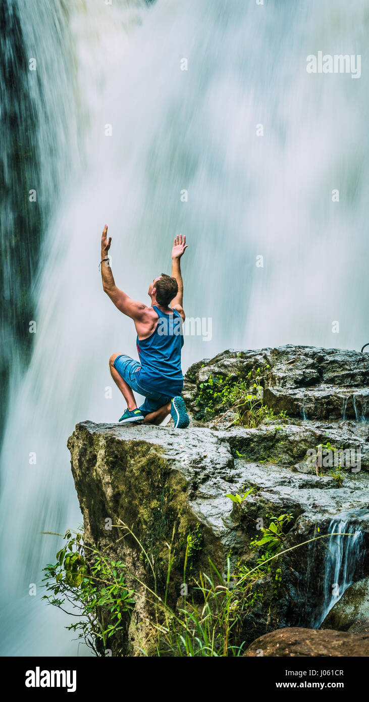 Man sitting in Front of Tegenungan Waterfall near Ubud raising hands and rhapsodize it, Bali, Indonesia Stock Photo