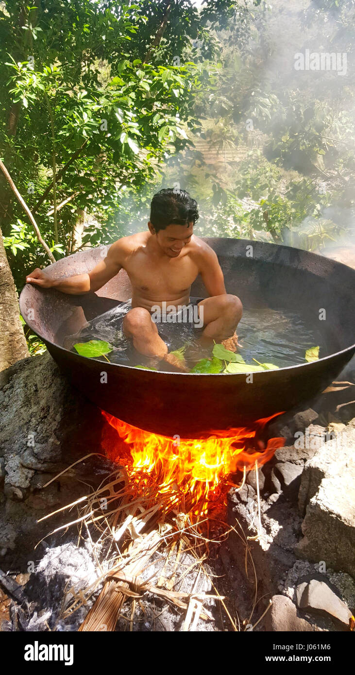 TIBIAO, ANTIQUE: STUNNING pictures have emerged showing a man looking like he is being cooked alive inside a huge cauldron above an open fire. The incredible images show a tourist putting on a brave face as he sits in a hot metal tub in an idyllic location. In one photo the flames appear to rise above the edge of the tub and flicker near his face. The snaps were taken in Tibiao, Antique by accountant Michael Diez from Manila, Philippines as he enjoyed a quick visit to the country. Stock Photo