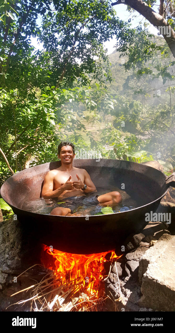 TIBIAO, ANTIQUE: STUNNING pictures have emerged showing a man looking like he is being cooked alive inside a huge cauldron above an open fire. The incredible images show a tourist putting on a brave face as he sits in a hot metal tub in an idyllic location. In one photo the flames appear to rise above the edge of the tub and flicker near his face. The snaps were taken in Tibiao, Antique by accountant Michael Diez from Manila, Philippines as he enjoyed a quick visit to the country. Stock Photo