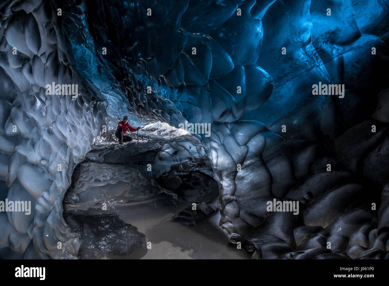 ICELAND: THESE cold-as-ice explorers were-willing-to-sacrifice in order to capture these magnificent ice caves before they melt away. Stunning images have revealed ice-cool British tourists chilling out inside Europe’s largest glacier – despite being at risk of flooding. The spectacular collection of images show the explorers braving the freezing temperatures to climb, photograph and even abseil down the inside of the icy cliff sides.  Another image shows one visitor on his knees appearing to pray next to a water fall of melted ice.  Other glistening shots show an adventurer trying to keep war Stock Photo