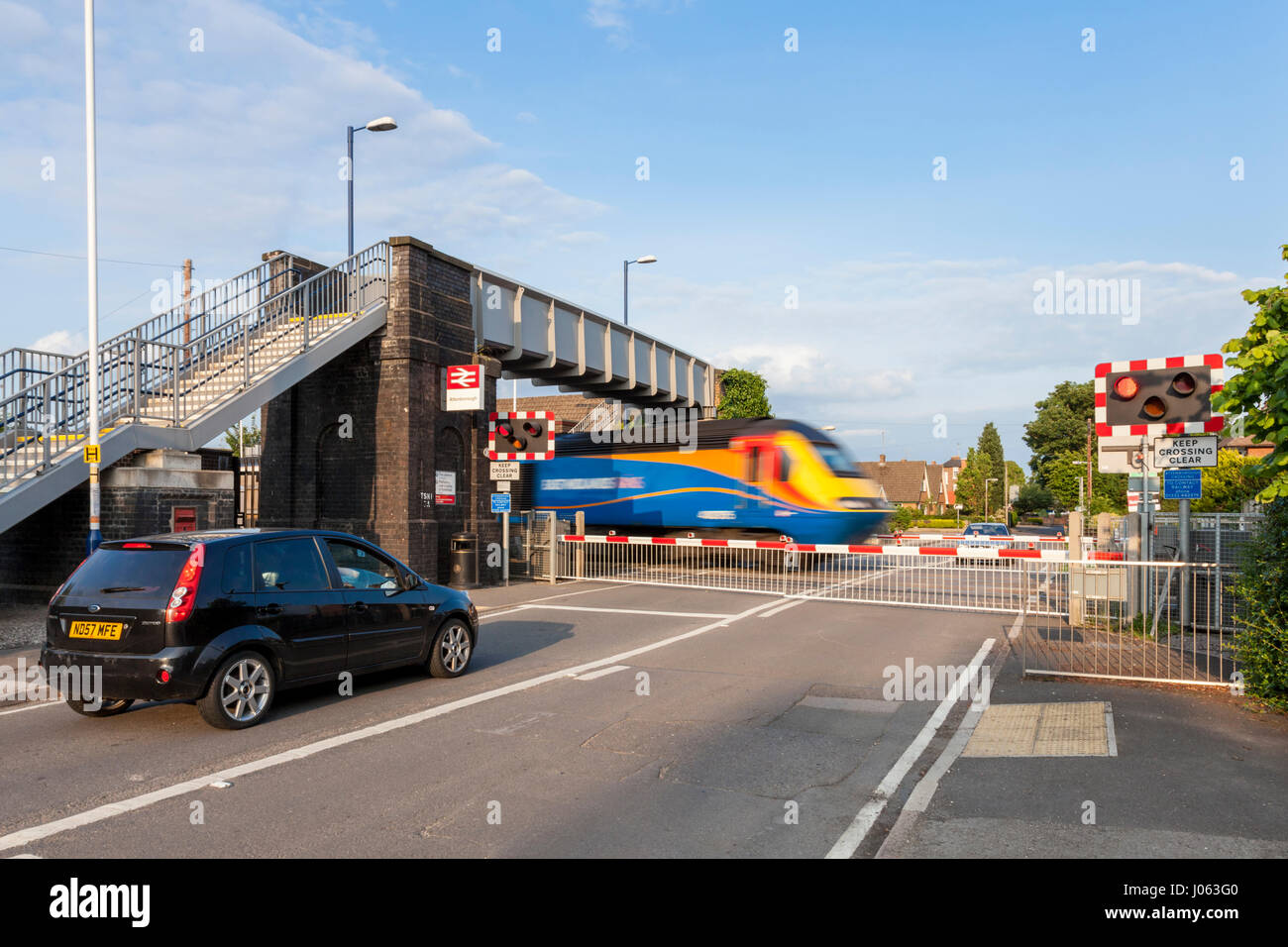 Cars waiting at a level crossing with the barriers lowered as a train passes. Attenborough Railway Station, Nottinghamshire, England, UK Stock Photo