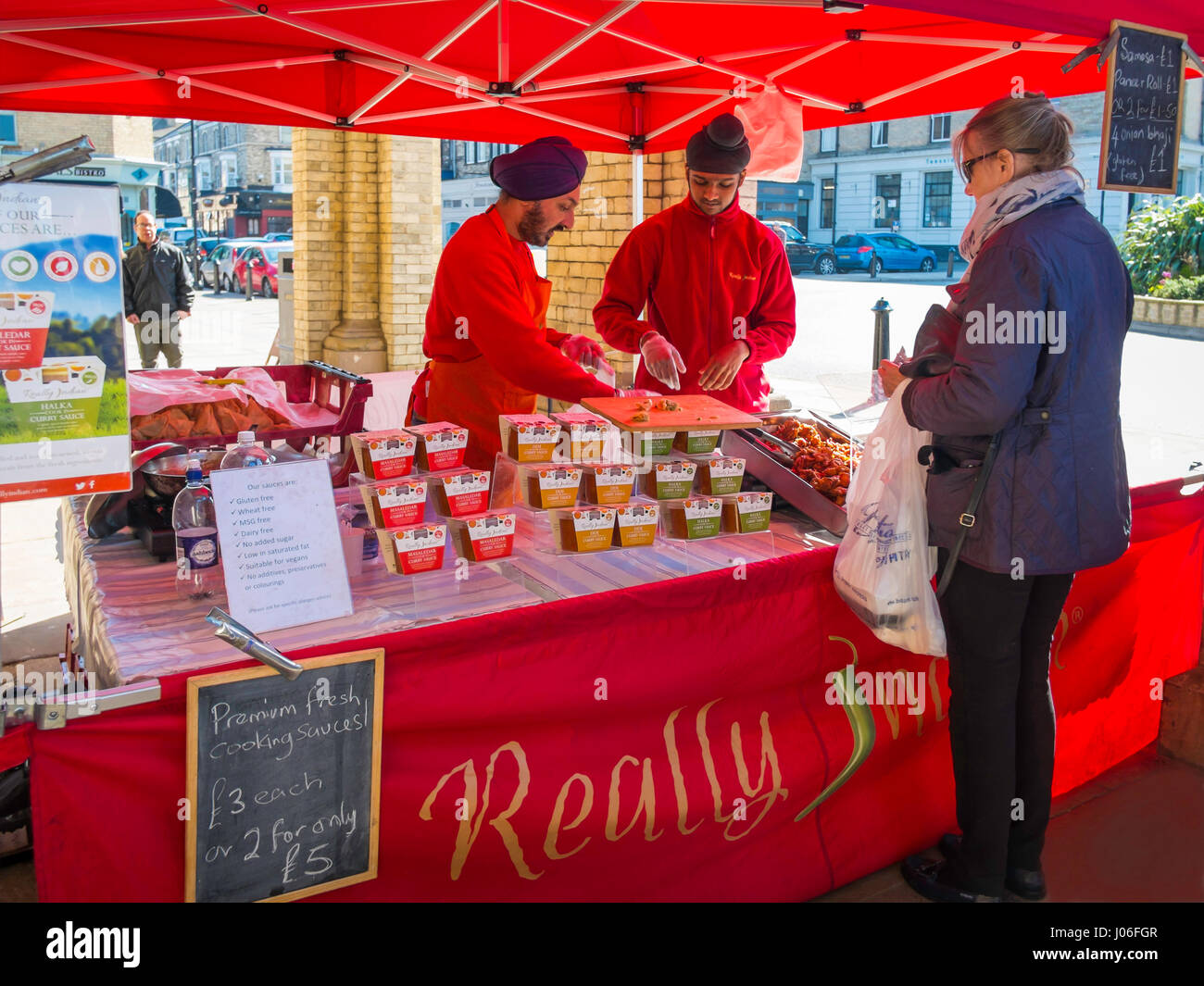 An woman buying Indian Food from Sikh  stall holders at a UK Farmer's market serving Curry Sauces and cooked 'Really Indian' food Stock Photo