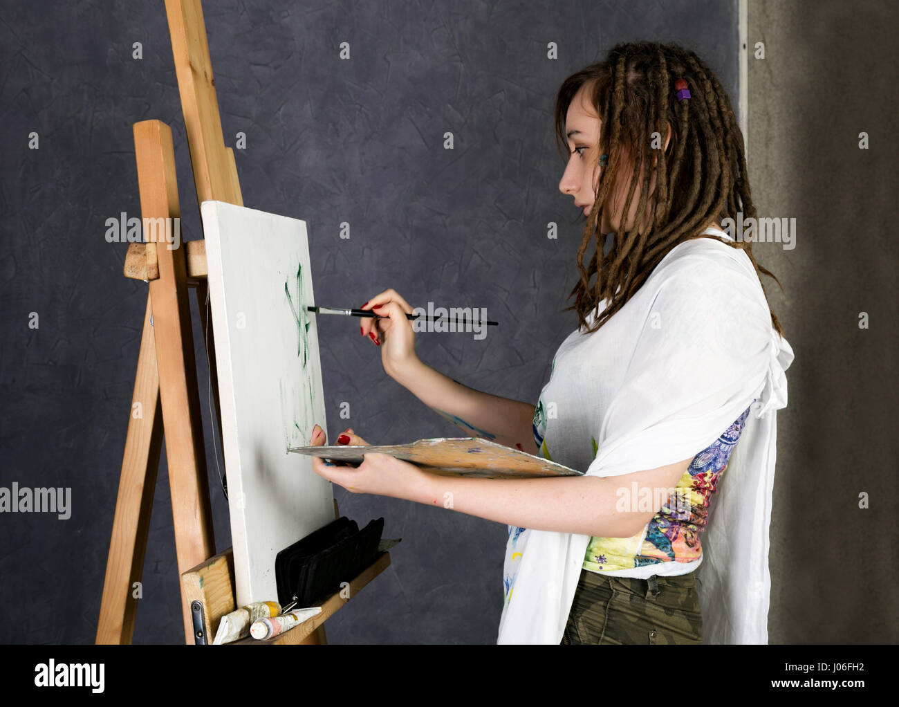 female paint artist posing next to a easel and paints on an canvas ...