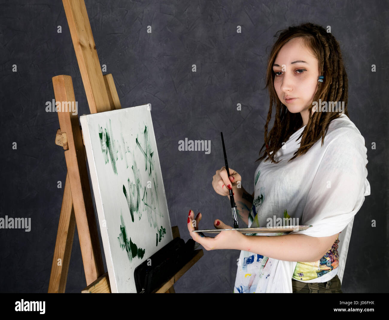 female paint artist posing next to a easel and paints on an canvas ...