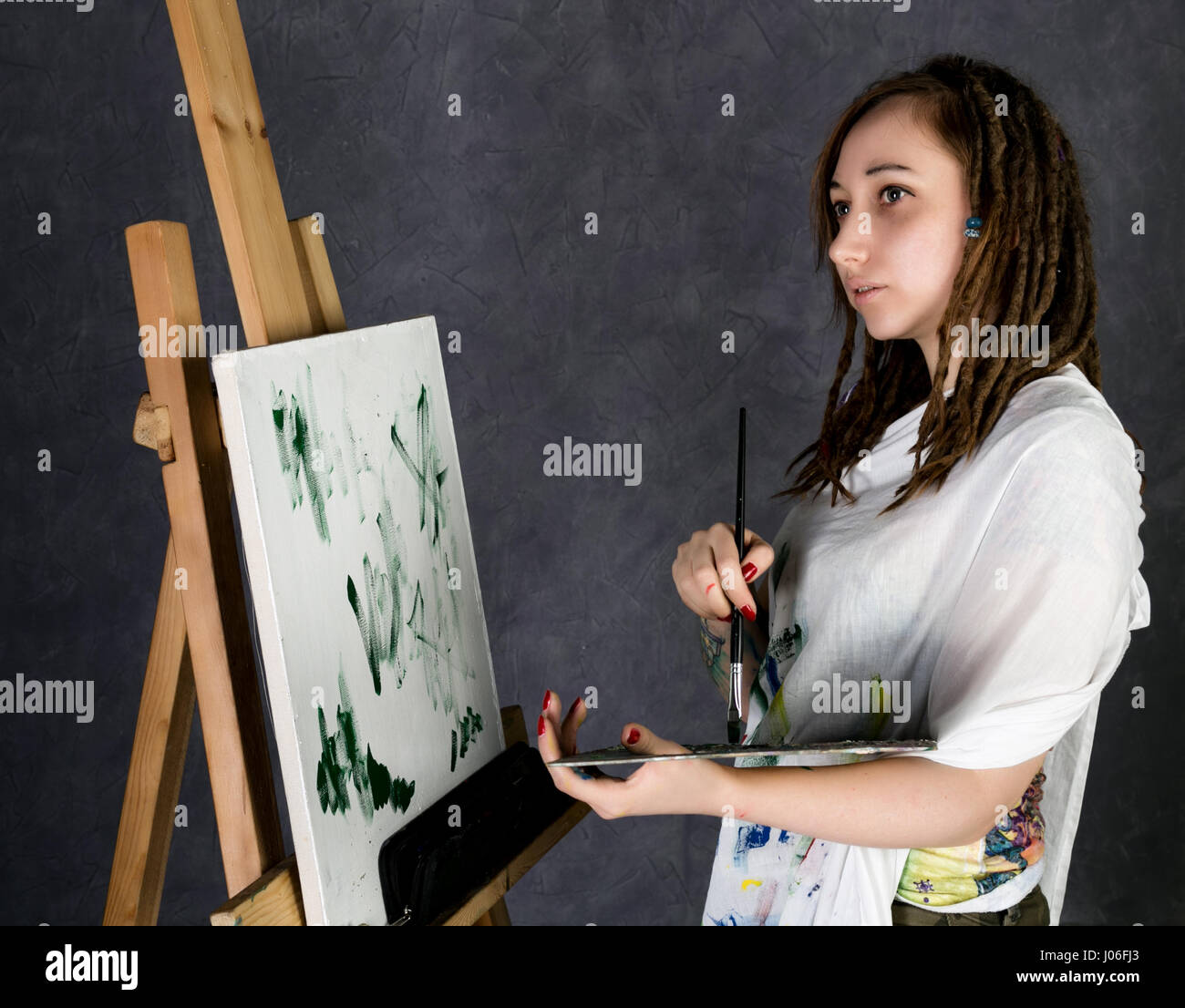 female paint artist posing next to a easel and paints on an canvas ...