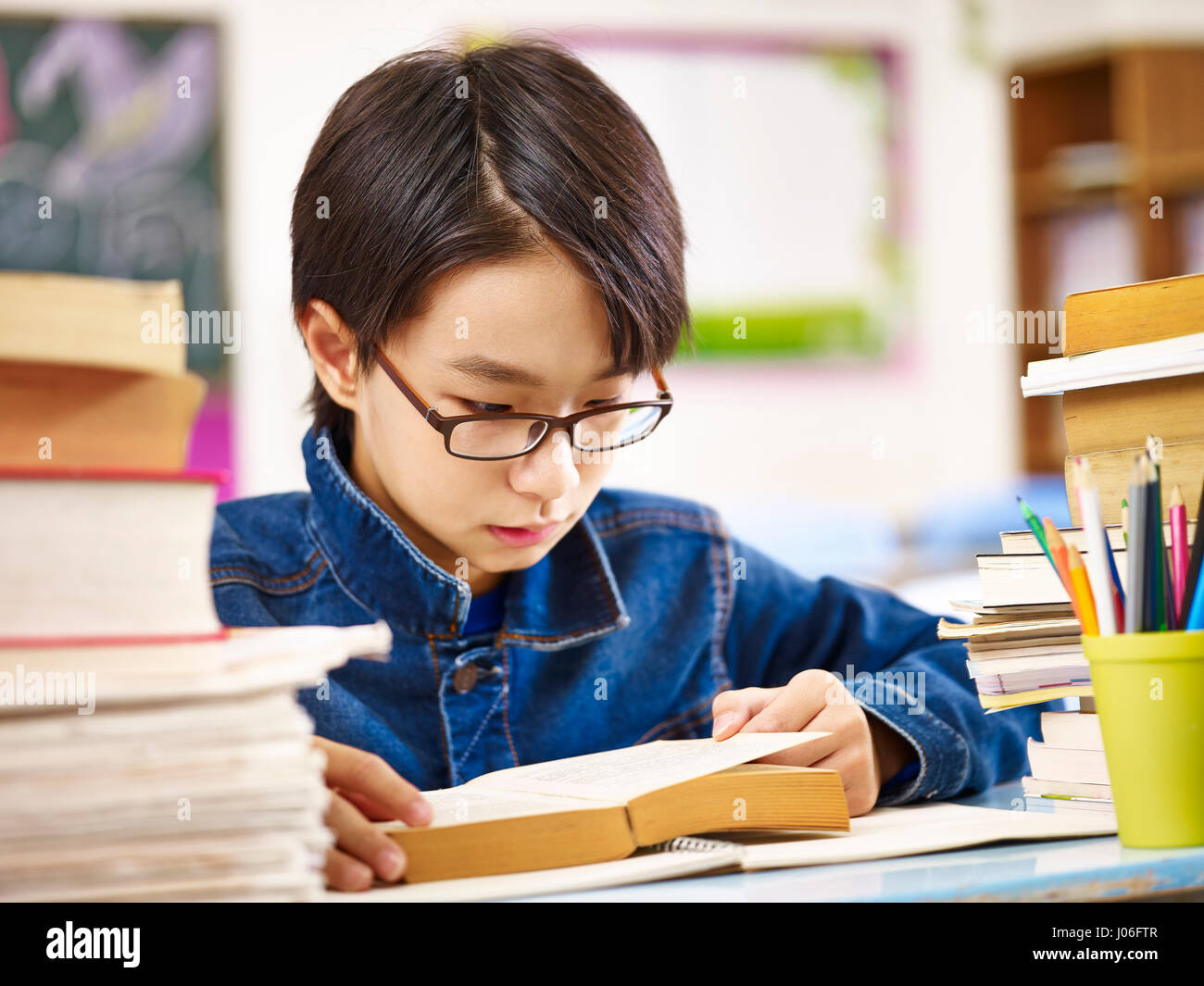 asian elementary school boy wearing glasses reading a thick book. Stock Photo