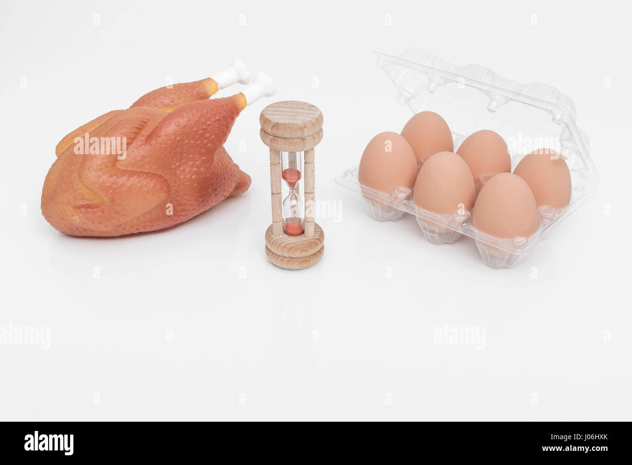 Wooden egg timer with box of eggs and replica chicken - as metaphor for that age-old question of which came first - chicken or egg. Stock Photo