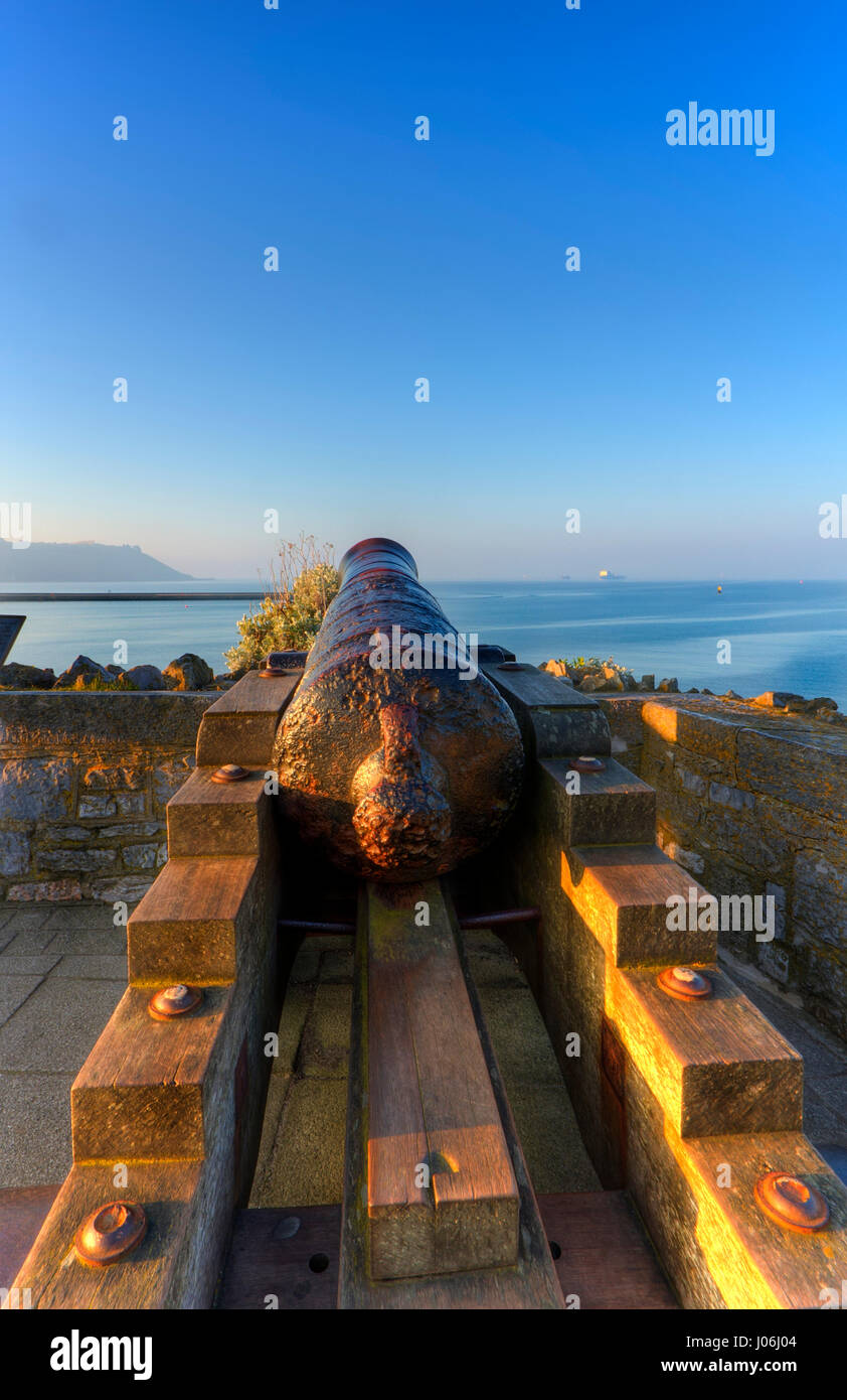 An old cannon sits looking out over Plymouth Sound with the early morning sun rising to the left and a slight sea mist in the distance. Stock Photo