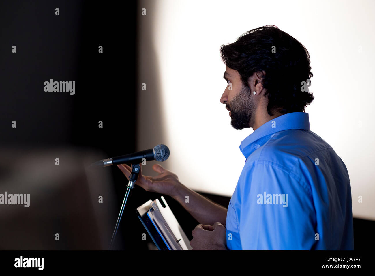 Male teacher making a speech in a lecture hall. He is standing at the podium and smiling to the crowd. Stock Photo