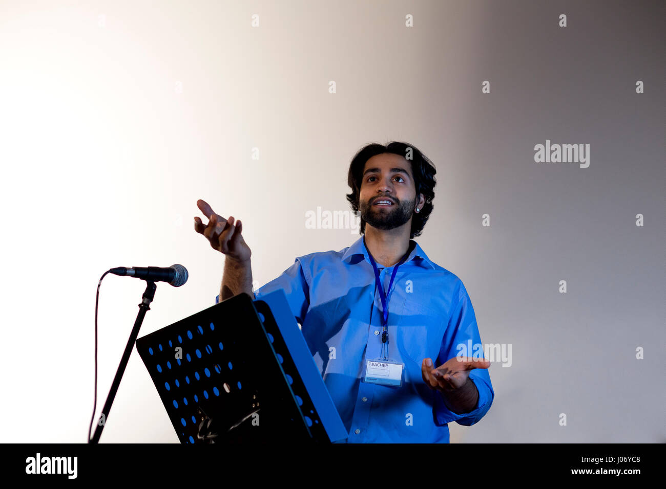 Male teacher making a speech in a lecture hall. He is standing at the podium and smiling to the crowd. Stock Photo