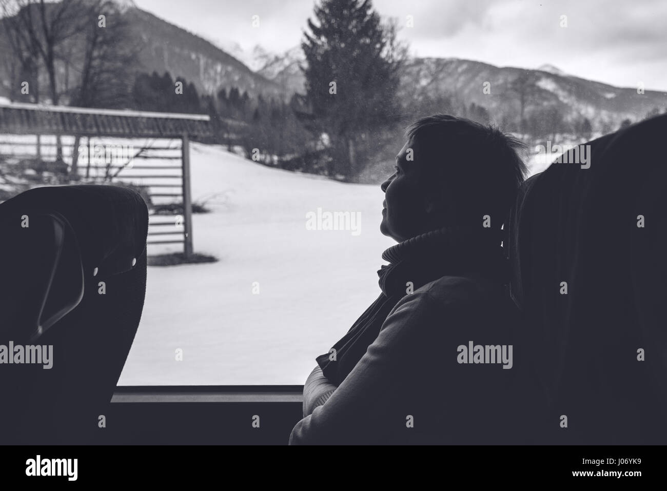 Female tourist on the bus riding through winter mountain landscape, monochromatic black and white image Stock Photo