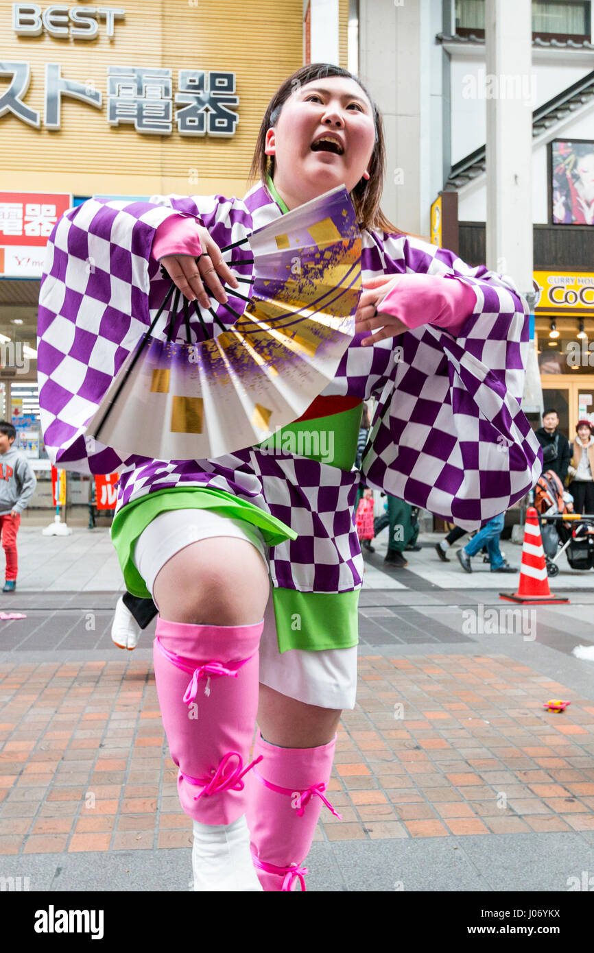 Japan, Kumamoto, Hinokuni Yosakoi dance festival. Teenage woman dancer, holding fan, in check pattern yukata, dancing in front of viewer. Close up. Stock Photo