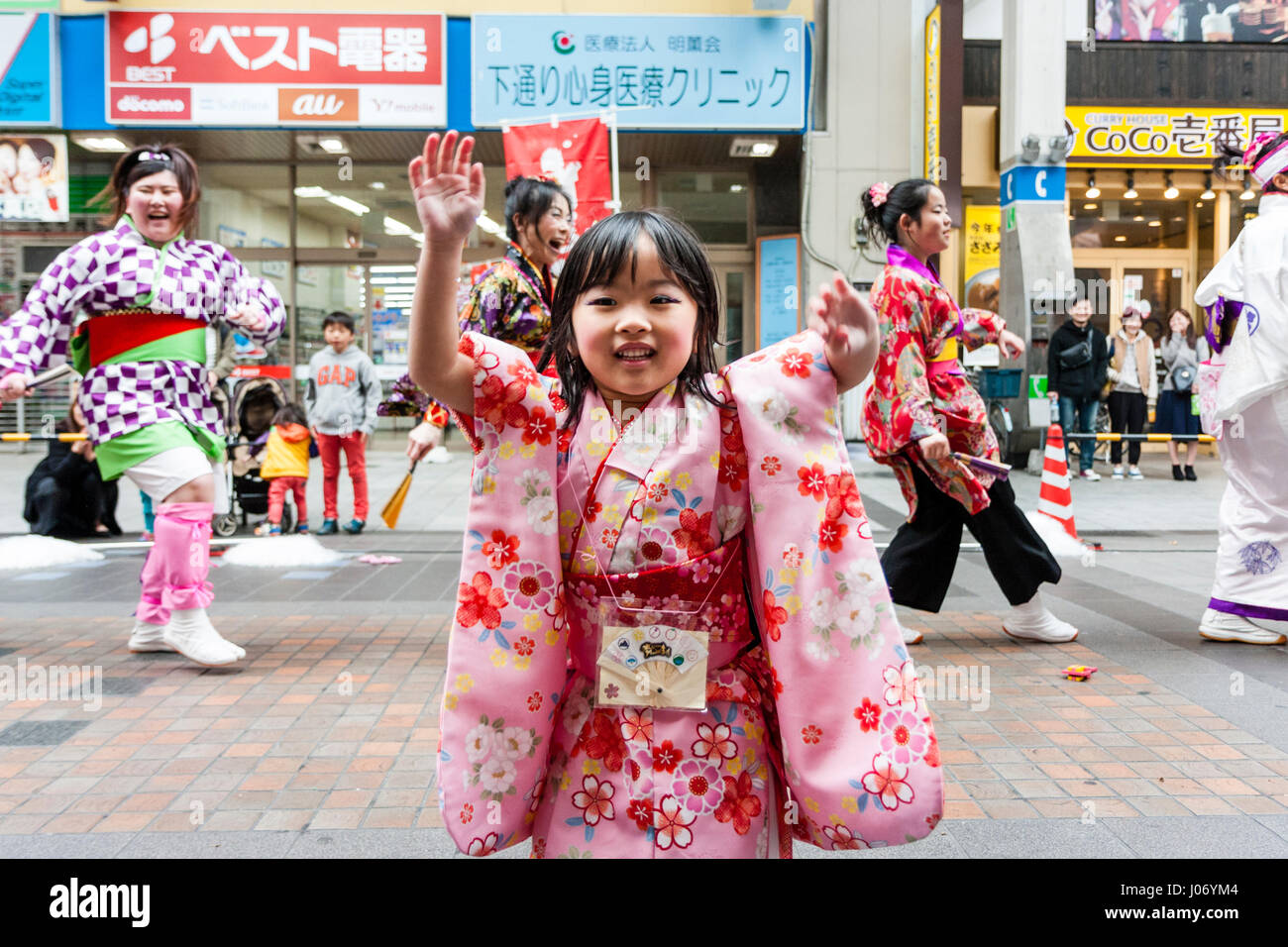 Japan, Kumamoto, Yosakoi dance festival. Close-up. Little smiling girl in pink kimono dancing in shopping mall with dance team behind her. Eye-contact Stock Photo