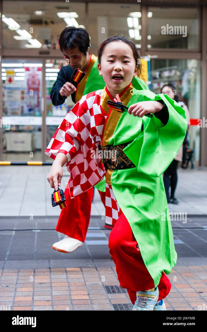Japan, Kumamoto, Hinokuni Yosakoi dance festival. Girl child dancing in green and red yukata, and using naruko, bird clappers. Close-up, eye-contact. Stock Photo