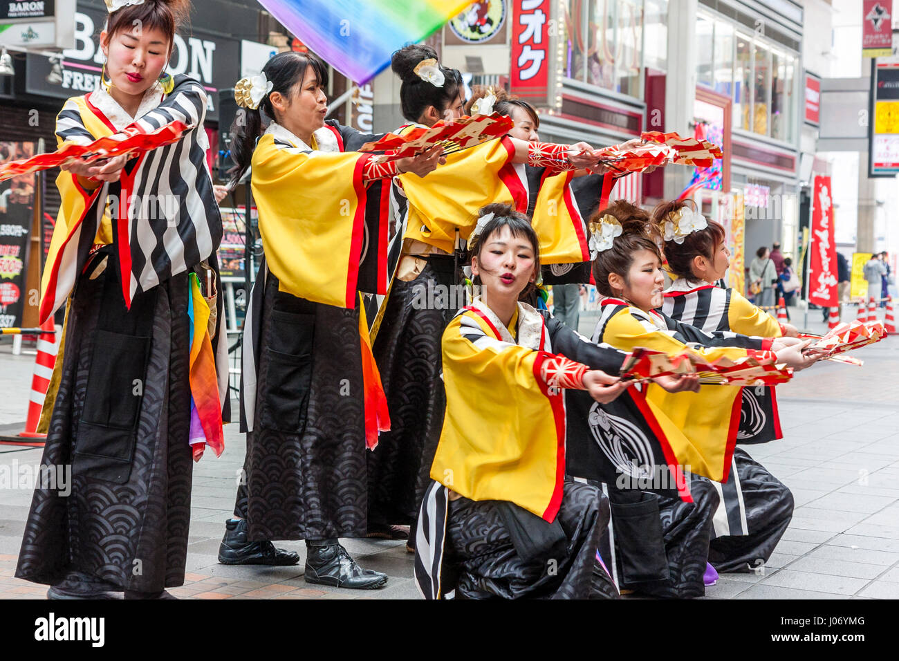Japan, Kumamoto, Hinokuni Yosakoi dance festival. Teenage women team, wearing black and yellow yukata, kneeling and holding fans, in shopping mall. Stock Photo