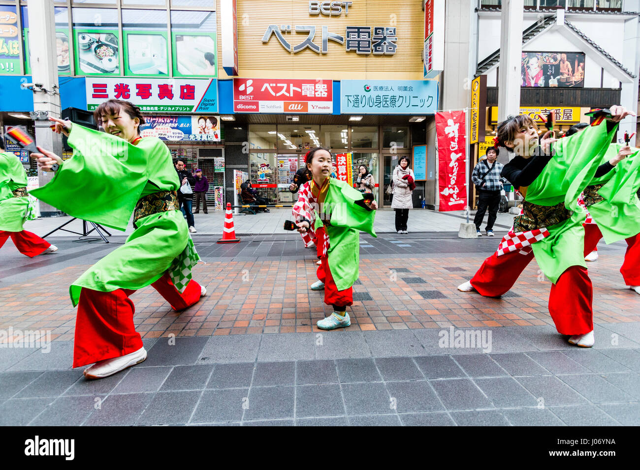 Japan, Kumamoto, Yosakoi dance festival. Dance team in colourful yukata, 2 men on either side, young teenage girl dances in middle, eye-contact. Stock Photo