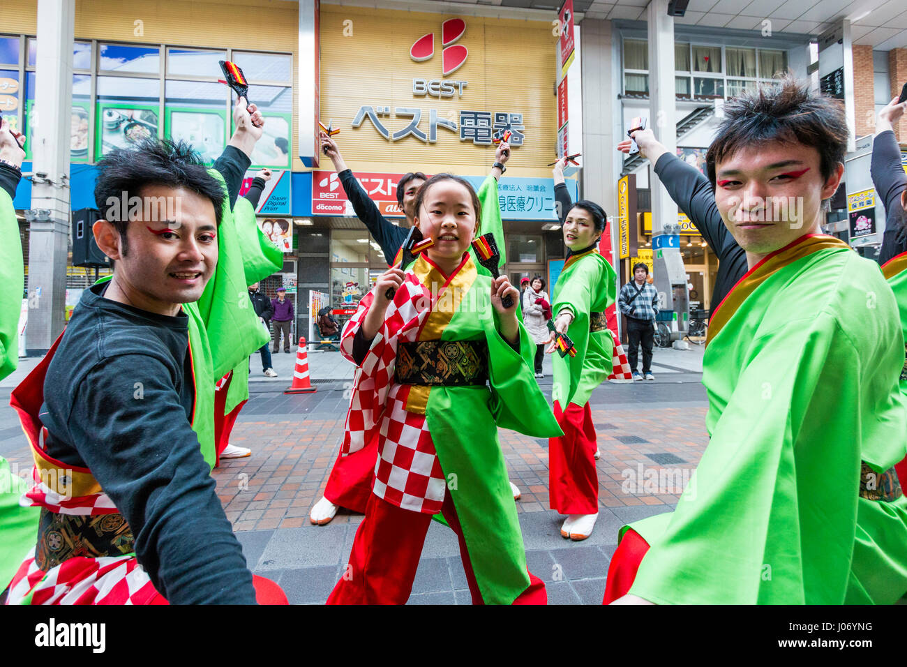Japan, Kumamoto, Yosakoi dance festival. Dance team in colourful yukata, 2 men on either side, young teenage girl dances in middle, eye-contact. Stock Photo