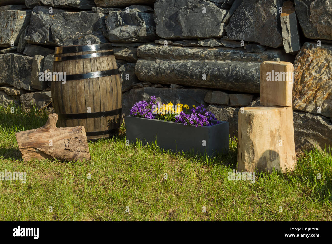 Oak wine barrel, handcrafted wood stool, pot of violets and bell flowers with a natural wall of rocks as background Stock Photo