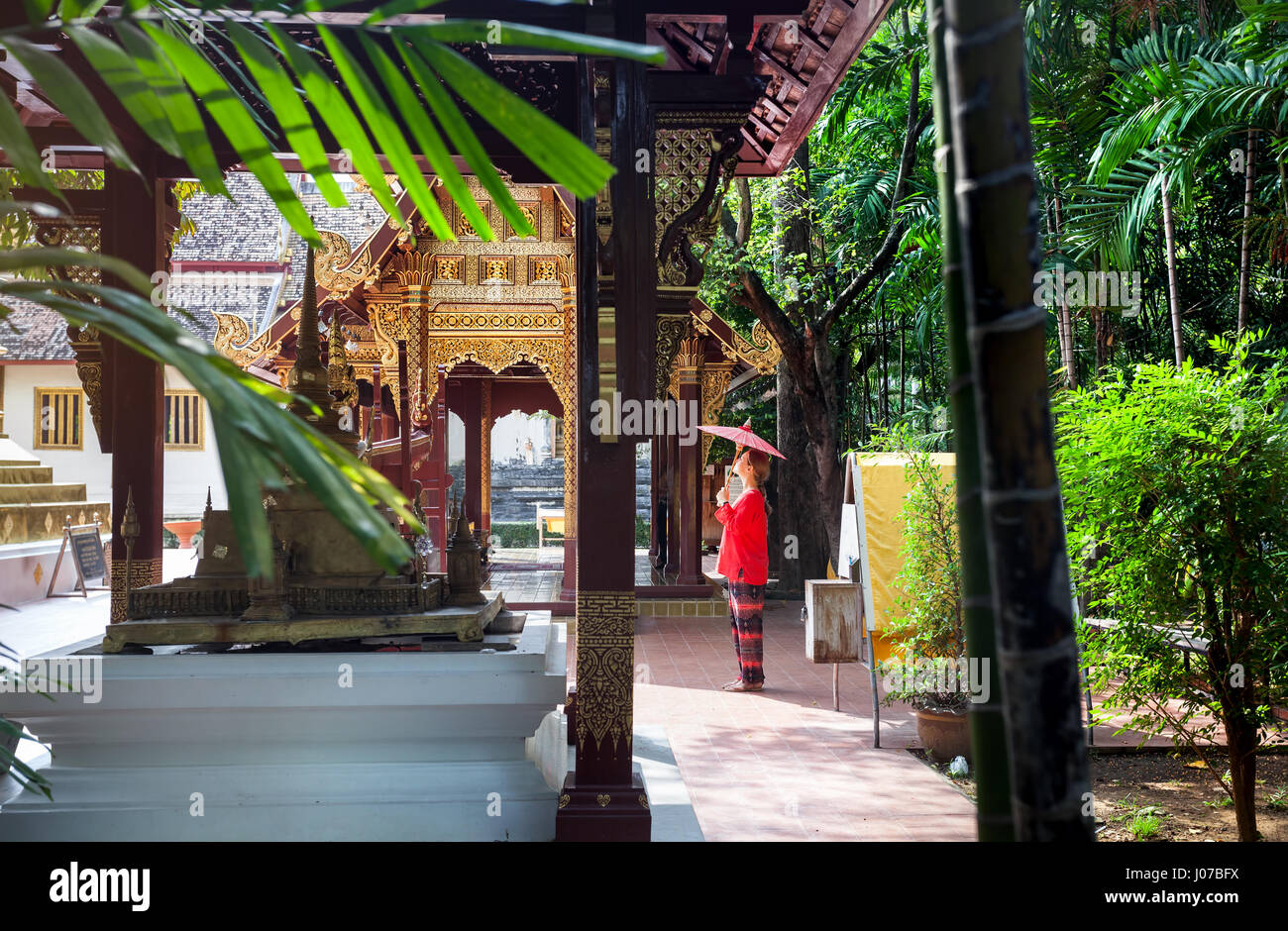 Woman tourist with red traditional Thai umbrella near Golden temple Wat Phra Singh in Chiang Mai, Thailand Stock Photo