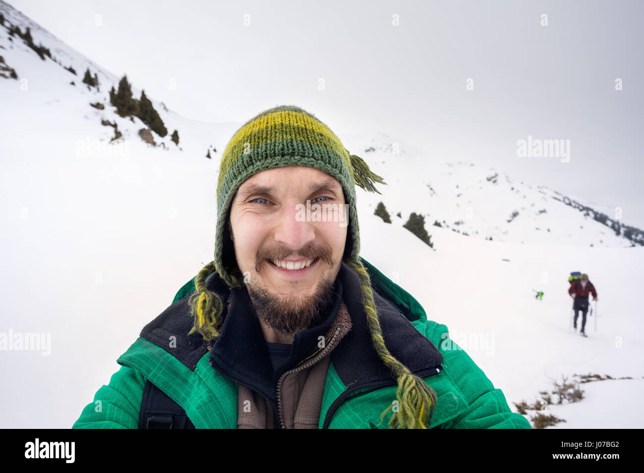 Selfie portrait happy bearded man in green jacket at snowy mountains Stock Photo